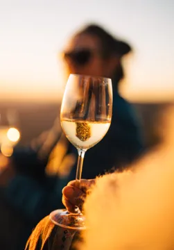 A glass of white wine held up in evening light, a person out of focus behind