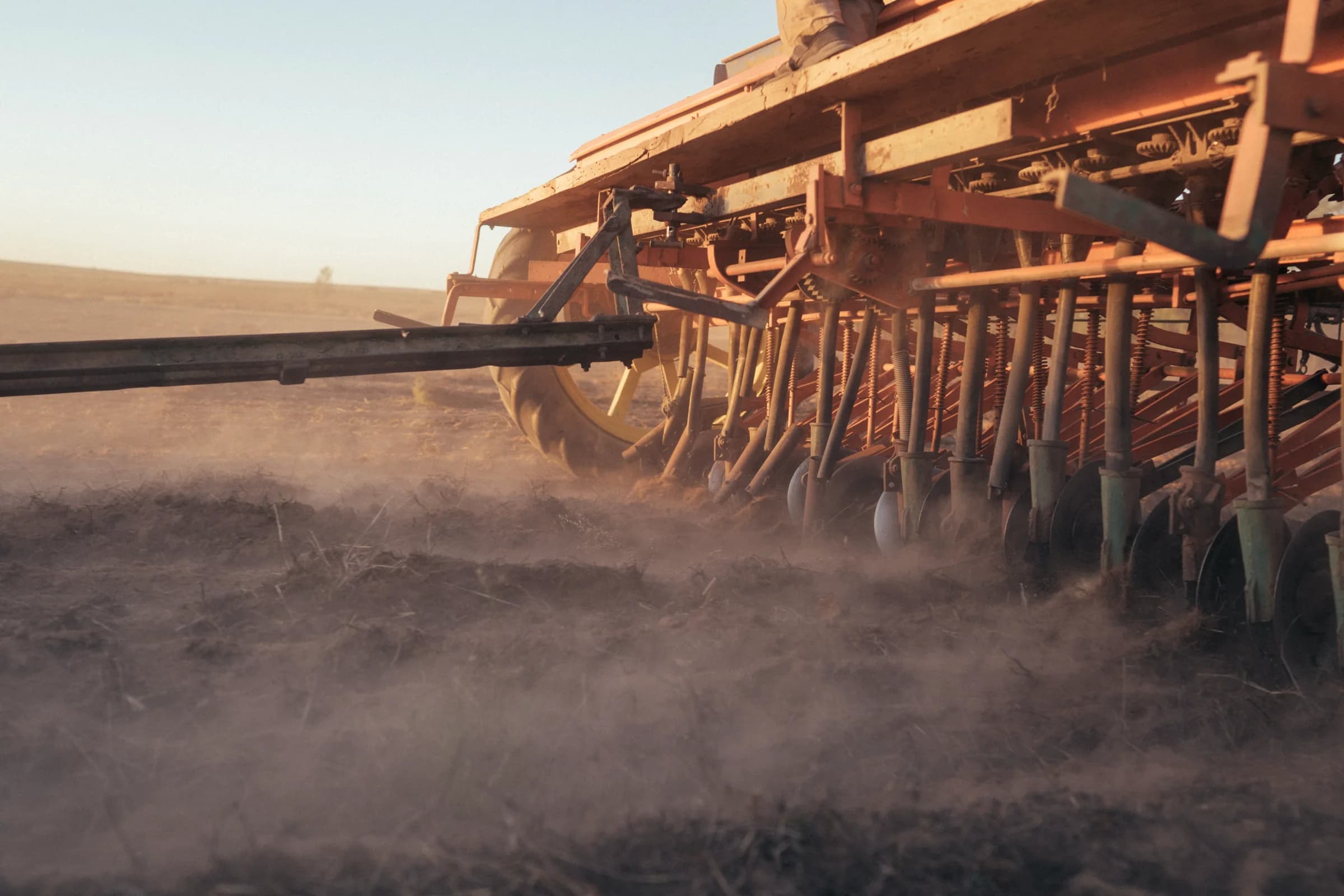 A close view of a planter's tines and discs raising dust in low sun